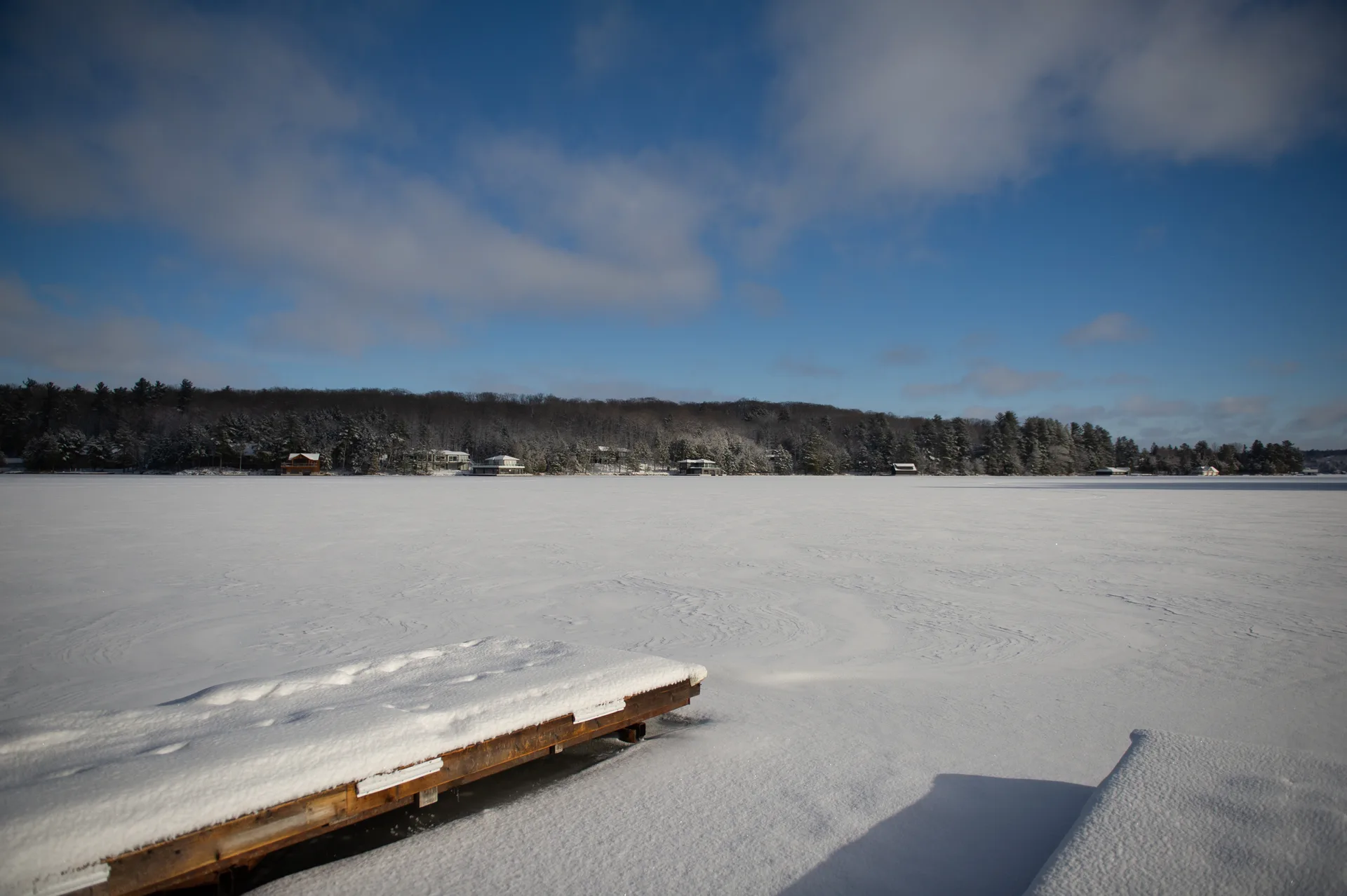 Snow-covered dock on a frozen lake ringed by winter forest