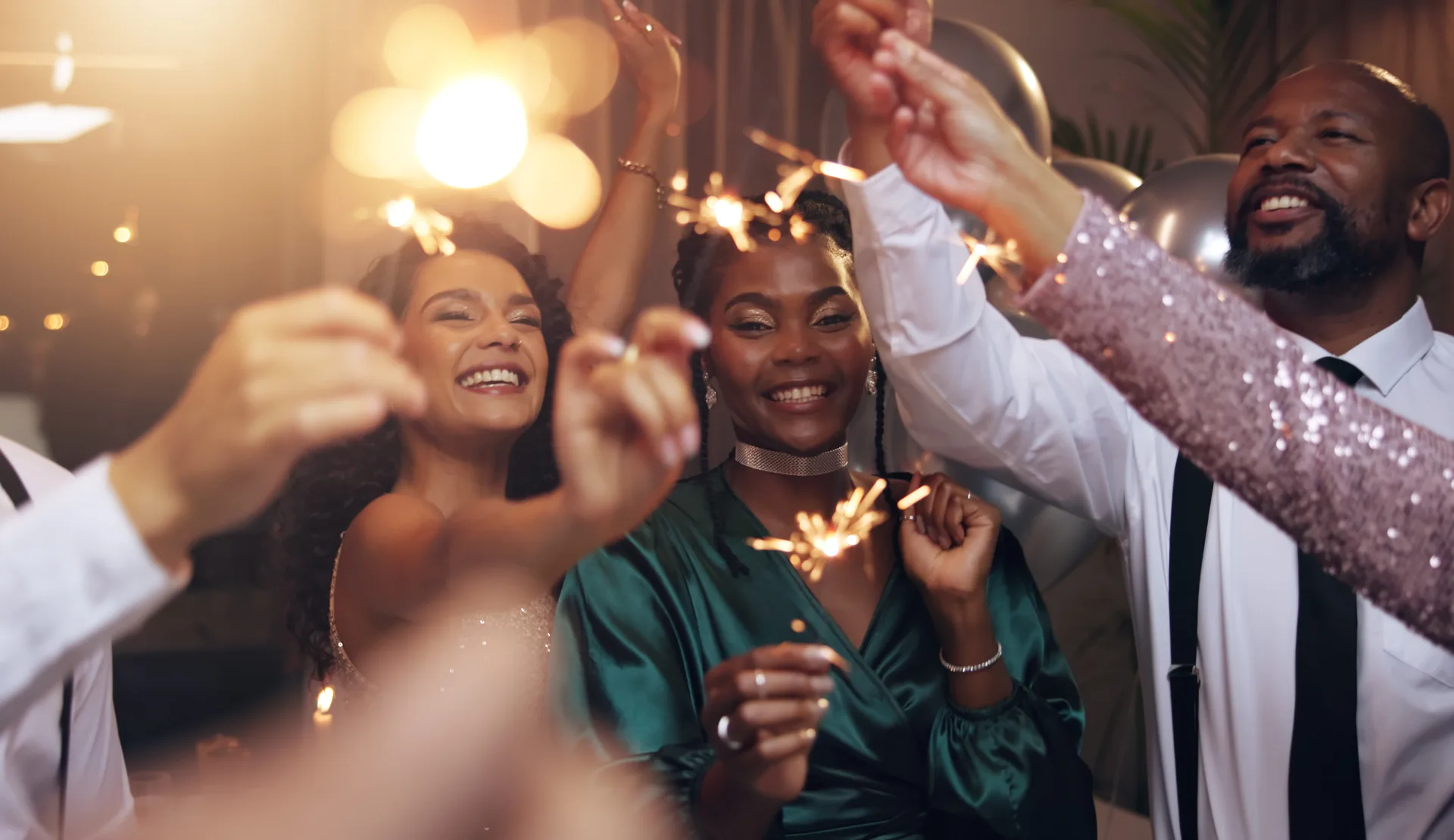 Friends in party dress raising lit sparklers at an evening celebration