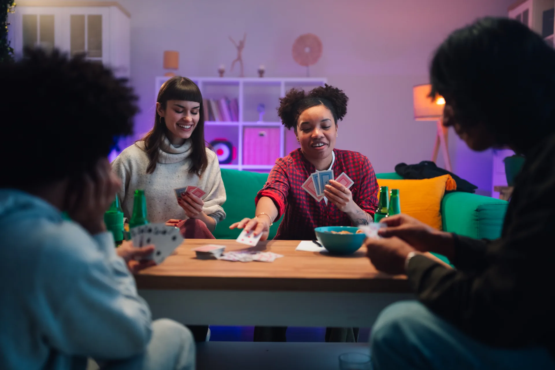 Four friends playing cards and drinking beer around a wooden table in a living room