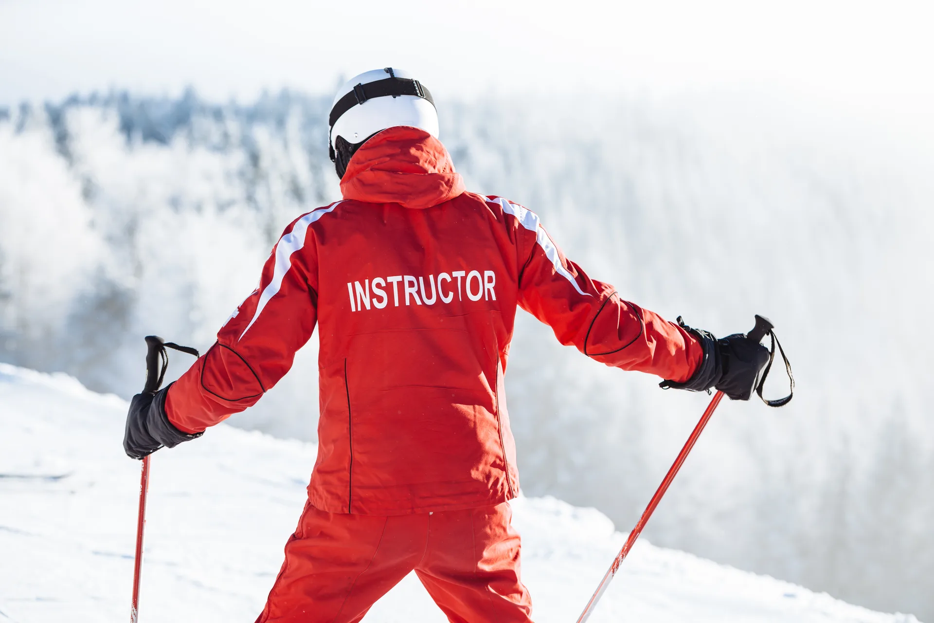 Ski instructor in a red jacket facing frosted trees on a ski slope