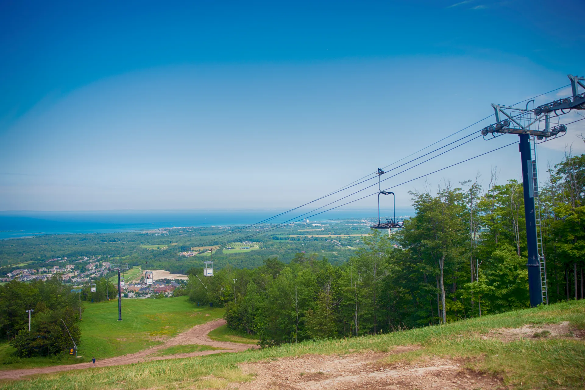 Chairlift towers above Blue Mountain's green summer slopes with Georgian Bay and Collingwood in the distance