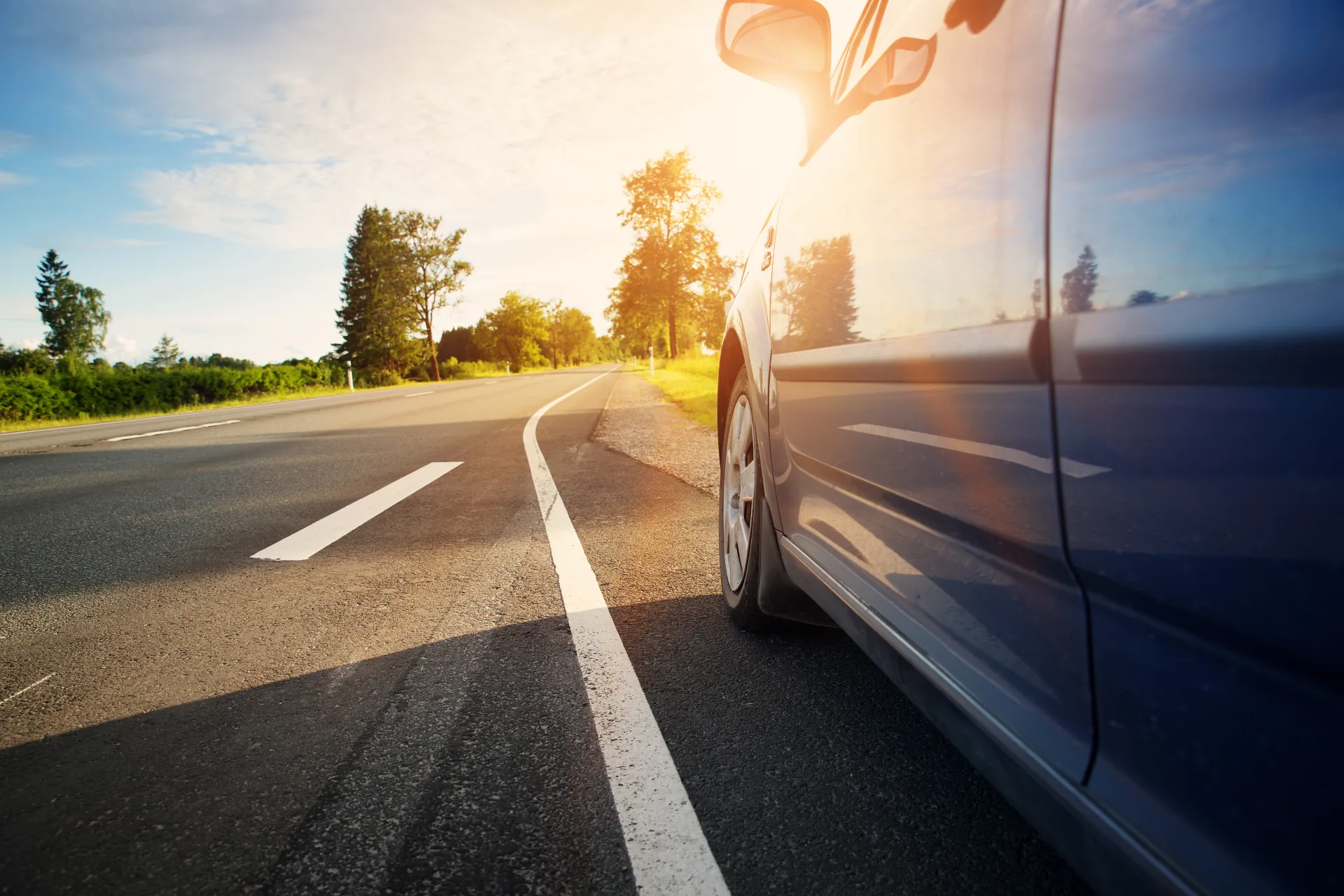 Car travelling a sunlit highway lined with summer trees